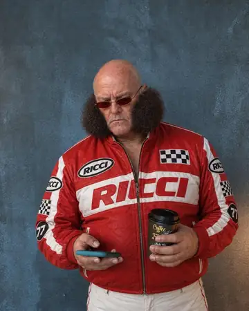 Rocco con cara seria frente al celular, con un café en la mano